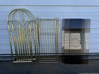 Full lot photo showing brass side panels, shelf frames and smoked glass panes leaning against a wall, unassembled.