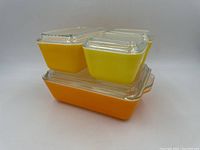 Four Pyrex Daisy Citrus Fridgies stacked showing orange and yellow glass containers with clear ribbed lids