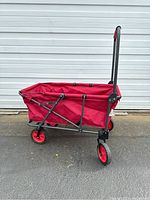 Red utility wagon with fabric sides on collapsible metal frame, front view showing handle and front wheel.