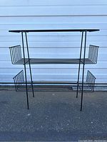 Full frontal view of the wrought iron plant stand showing the two tiered shelving and basket side holders