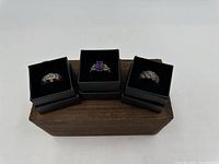 Photo of three rings displayed in black jewelry boxes on a wood block
