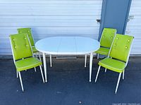 Full view of four lime green upholstered Howell West dining chairs arranged around white oval laminate dining table outdoors on pavement.