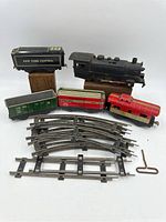 Full view of vintage Marx tin litho windup train set components including locomotive, tender, three train cars, track pieces, and windup key.