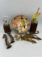 Full lot showing Fitz and Floyd mug, Opal House bird bowl, brass peacock hooks, brass-tone peacock handles, ceramic bird salt & pepper shakers, and ceramic parrot figurine.