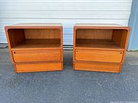 Front view of both nightstands side by side on pavement with open shelves and drawers visible
