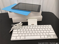 Apple iPad 2 and keyboard dock with USB cable and two boxes shown stacked on a black surface.