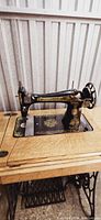Singer treadle sewing machine in black with gold sphinx design on the arm, mounted in wood cabinet.