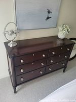 Front angled view of dresser showing six drawers, silver tone hardware, dark mahogany finish, and decorative tapered legs.