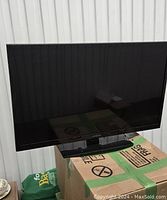 Full view of black 32-inch flat screen with stand, placed on cardboard box.