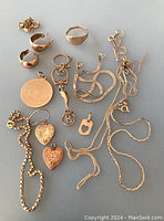 Multiple jewellery pieces laid out on grey background, including chains, charms, earrings, bracelet.