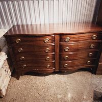 Full view of mahogany bow front dresser with eight drawers and brass pulls arranged symmetrically.