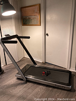Photo of silver and black SuperFit treadmill standing unfolded on floor with remote control on running belt.