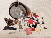 Group shot of Allan doll in light blue outfit, round travel case and assorted clothing items