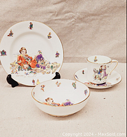 Full view of the complete four-piece set: plate, bowl, teacup, and saucer showing the colorful illustrations and gold trim.