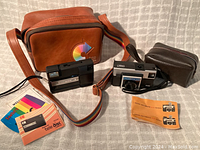 Photo showing the caramel brown Kodak tote bag with rainbow woven strap, Kodak TeleDisk camera, Kodak Instamatic X-15 camera, small black pouch, pamphlets, and additional strap and pouch.
