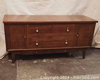 Front view of mid-century cedar chest showing two side cabinet doors, central drawer with four white turn handles, and two lower drawers with small round knobs. Rectangular box shape on tapered legs.