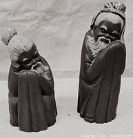 Pair of matte grey Lladro figurines depicting Chinese men with white detailed hair and beard, standing side by side.