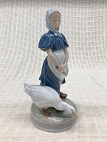 Front view of Royal Copenhagen porcelain figurine of girl with goose, highlighting blue dress, white apron, and goose beside her.