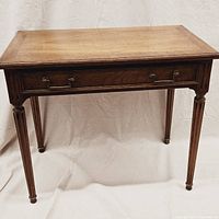 Front view of rectangular wooden writing desk showing two metal-pulled drawers and fluted legs.