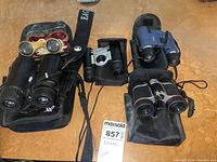 Overview of six binoculars on table showing different sizes, colors, and cases including one ornate vintage pair.