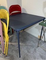 Black folding card table with metal legs, showing part of the legs and top surface in a basement setting.