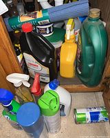 Wide view of assorted cleaning bottles and containers under kitchen sink, showing various spray bottles and containers in different colors.