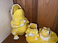 Three yellow spotted ceramic frog figurines placed against a wooden backdrop.