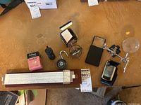 Photo showing a collection of optical tools and scientific items including the Versalog slide rule, gyroscope, magnifiers, and a combination lock on a wooden table surface.