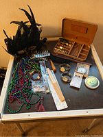 Full lot showing black feather mask, beaded necklaces, bracelets, wooden object, watch box and various small items