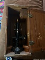 Antique microscope inside open wooden case with locking hinges and padding