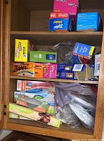 Kitchen cabinet shelf showing multiple boxes of plastic zipper and storage bags, some opened and partially used.