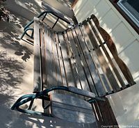 Top angled view of wood slat porch swing with metal armrests and frame on porch floor.