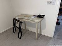 Small white wooden desk with single drawer and a tray organizer on top, a black luggage rack hanging on side