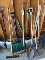 Photo showing assortment of garden and snow tools including rakes, shovels, and hoe.