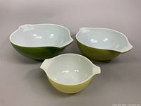 Front and top view showing the three glass mixing bowls in green and yellow with white interiors and dual handles with pouring spouts.
