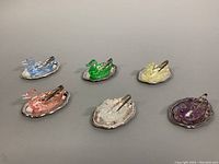 Photo showing the full set of six geometrically carved crystal duck salt cellars in various colors on silver-tone trays with tongs.