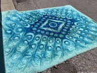 Full view of the rug laid on asphalt showing the entire pattern with areas of discoloration and stains.