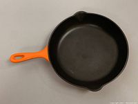 Top view showing round cooking surface and orange handle with two pour spouts.