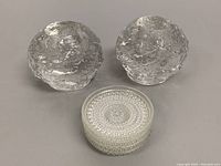 Pair of textured glass snowball candleholders alongside stacked clear glass coasters featuring a beaded circular pattern.