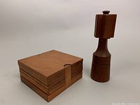 Photo showing stacked square teak coasters in holder next to the pepper mill shaker