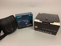 Nikon and Canon camera boxes with Canon SX610 HS box, Nikon Coolpix P7100 box, and black camera case