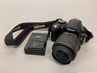 Front view of Nikon D3100 camera with attached lens and Nikon battery charger alongside.