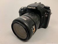 Front angle view of Pentax K10D with 28-80mm lens attached, showing lens mark and camera body details.