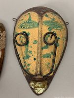 Front view of the ceramic tribal mask showing yellow and green wax resist glaze and patina metal wire accents