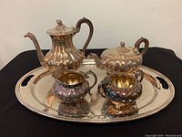 Five-piece silver plated tea set shown on black cloth. Includes coffee pot, teapot, creamer, sugar bowl on large tray.