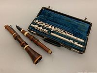 Vintage wooden clarinet disassembled into upper and lower parts, accompanied by a silver flute in a blue velvet lined hard case.