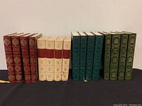 Photo of four antique/vintage French book sets in various covers: red, cream, green, and teal, arranged on a white shelf.