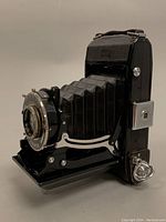 Side angle showing camera folded-out with bellows extended, metal lens and shutter assembly visible.