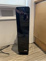 Front view of tall black GermGuardian air purifier with SmartHQ logo and reflective surface, plugged in with power cord on carpeted floor.