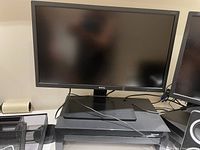 Two BenQ monitors displayed on a desk with visible cables, computer speakers, and a headset.